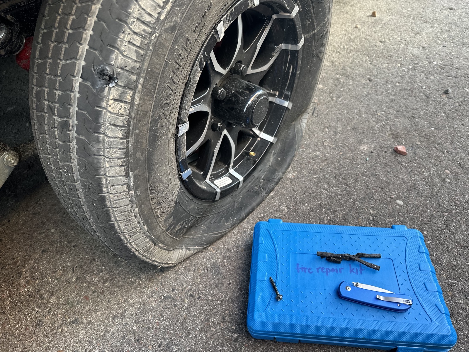 Flat trailer tire with plug repair kit open on the ground &mdash; found and repaired at pre-trip inspection